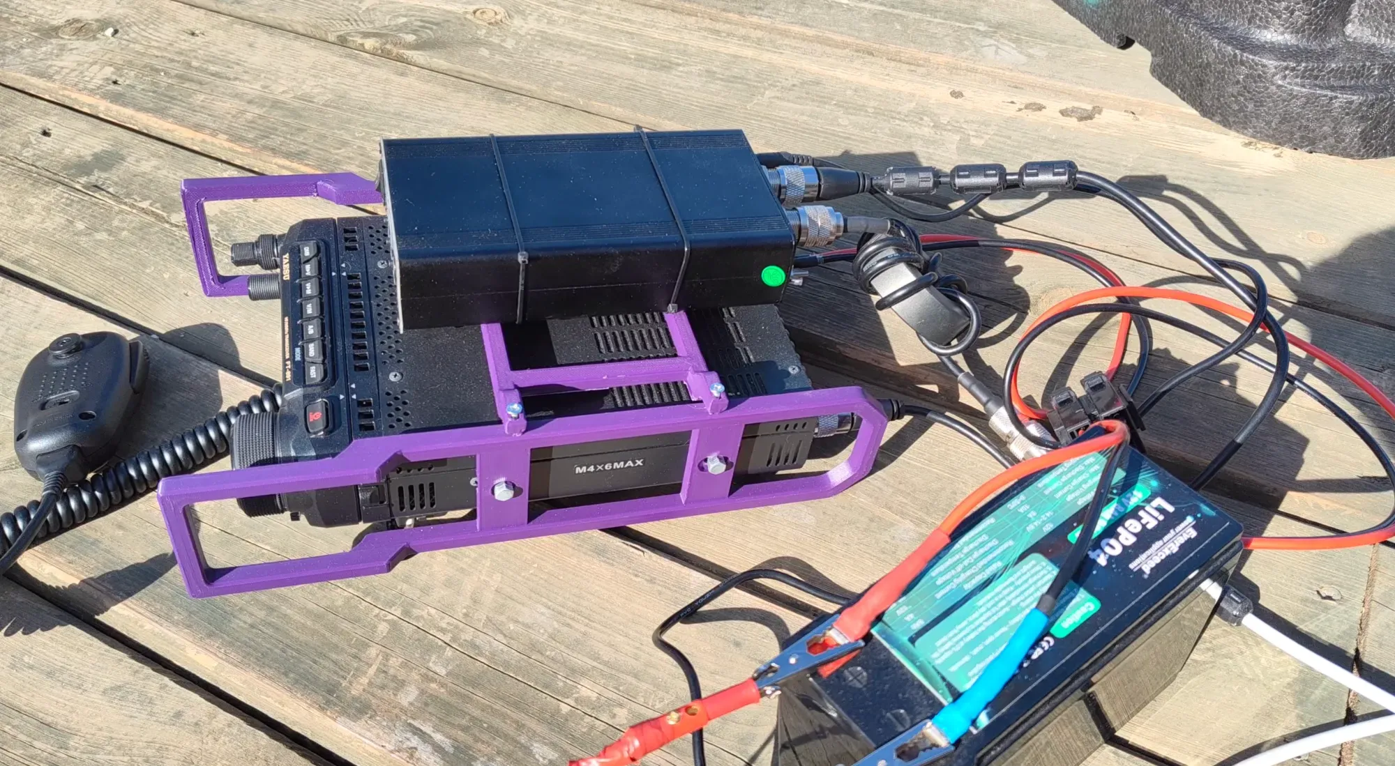 El Yaesu FT-891 en su soporte morado, con el acoplador ATU-130 encima y la batería LiFePO4 al lado, sobre una mesa de madera